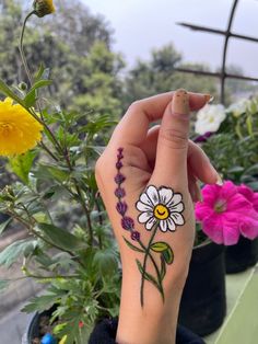 a woman's hand with a flower tattoo on her wrist and flowers in the background