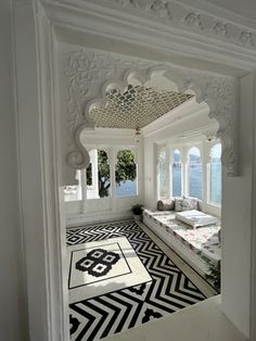 an ornate bedroom with white walls and black and white flooring, along with large windows