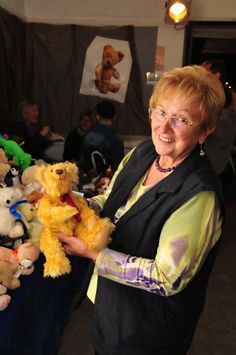 a woman holding a teddy bear in front of stuffed animals on a blue table cloth