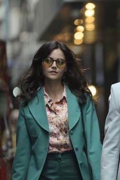 two people walking down the street in suits and sunglasses, one is wearing a green blazer