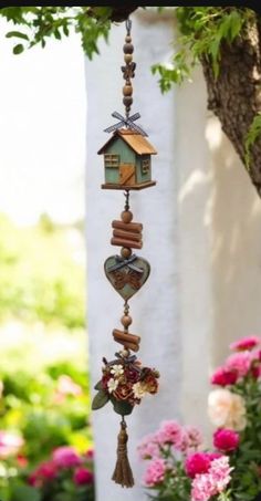 a wind chime hanging from a tree with flowers in the foreground and a house on it