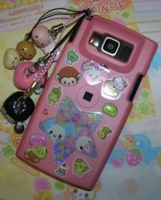 a pink cell phone with various stickers on it and a keychain attached to it