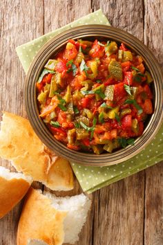 a bowl filled with lots of food next to bread on top of a wooden table