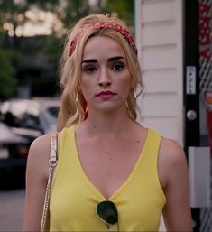 a woman in a yellow top is walking down the street with her hand on her hip