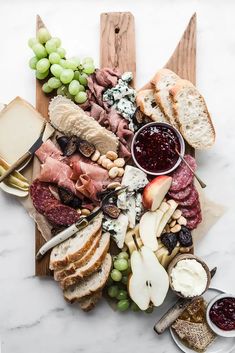 an assortment of cheeses, meats and fruit on a cutting board with bread