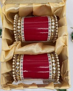 two red bracelets in a box with gold ribbon and pearls on the sides,