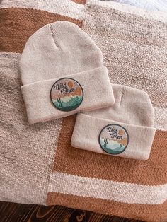 two white beanies sitting on top of a brown and white striped blanket next to each other