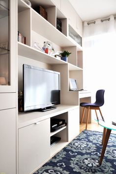 a flat screen tv sitting on top of a white shelf next to a chair and table