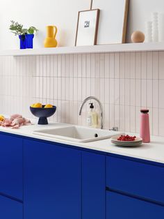 a kitchen with blue cabinets and white counter tops, pink tiles on the back wall