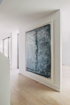 an abstract painting hangs on the wall in a white room with hardwood floors and walls