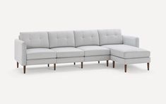 a white sectional couch with wooden legs and an ottoman on the bottom right hand side