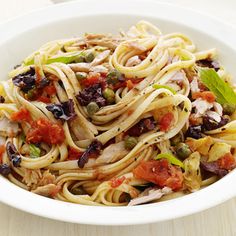 a white bowl filled with pasta and vegetables on top of a wooden table next to a fork