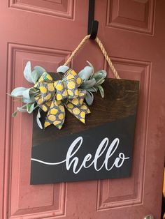 a wooden sign hanging on the side of a red door with a yellow and black bow