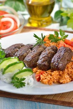 some meat and rice on a plate with cucumbers, tomatoes and sauces