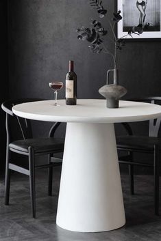 a white table with two black chairs and a bottle of wine on the table next to it