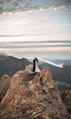 a bride and groom standing on top of a mountain