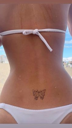 a woman with a butterfly tattoo on her lower back, standing in front of the ocean