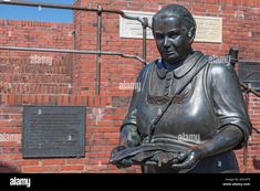 a bronze statue of a woman holding a tray in front of a brick wall with writing on it - stock image