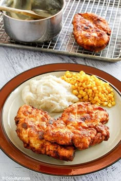 two pieces of chicken, mashed potatoes and corn on a plate next to a metal pan