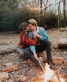 a man and woman sitting next to each other near a campfire in the woods