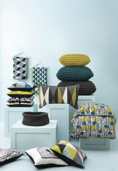 pillows and cushions are arranged on white pedestals in front of blue walls with geometric designs