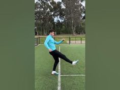 a man kicking a soccer ball on top of a green field with trees in the background