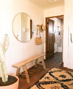 a wooden bench sitting in front of a mirror on a wall next to a potted cactus