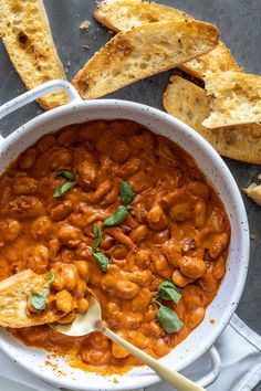 a white bowl filled with baked beans and bread on top of a gray countertop