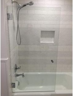 a bathtub with a glass shower door and white tile on the wall behind it