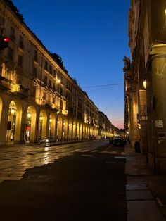 an empty city street at night with lights on and cars parked along the side walk