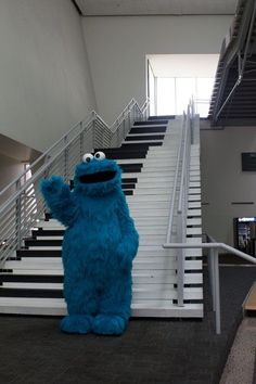 the sesame street character is standing in front of some stairs with his hand up and looking at the camera