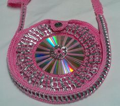 a pink crocheted purse with silver chains and a cd in the center on a white surface