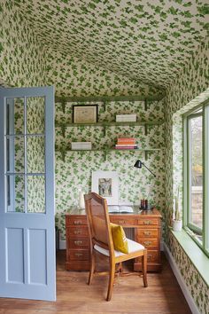 a chair and desk in a room with green wallpaper on the walls, along with an open door