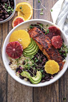 a white bowl filled with meat, beans and veggies on top of a wooden table