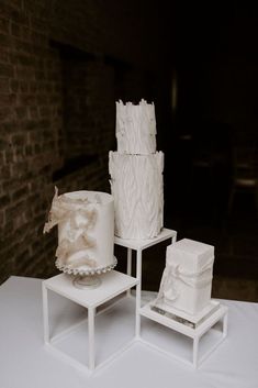 three white cakes sitting on top of each other in front of a brick wall and table