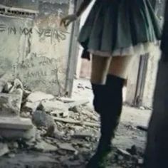 a woman in knee high boots standing next to a destroyed building with graffiti on the walls