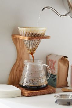 coffee being poured into a glass carafe on top of a wooden stand next to other items