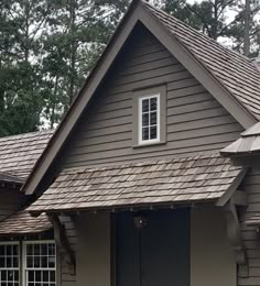 a brown house with a black door and windows on the front porch is surrounded by trees