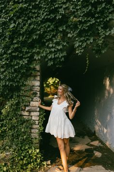 a woman standing in front of a wall with ivy growing up it's sides