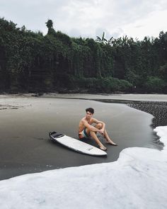 a man sitting on top of a surfboard in the sand