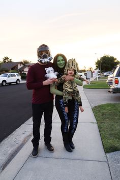 a man and woman are standing on the sidewalk with two children dressed up in costumes