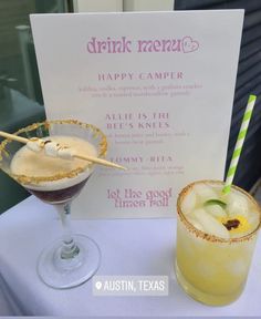 two cocktails sitting on top of a table next to a sign