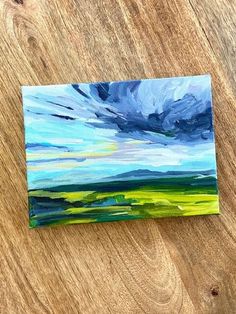 an acrylic painting of blue, green and yellow clouds on a wood surface