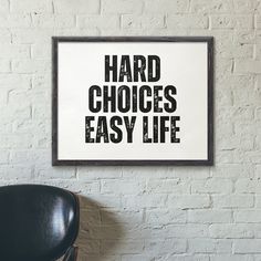 a black chair sitting in front of a white brick wall next to a sign that says, hard choices easy life