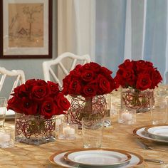 red roses in glass vases sitting on a table with white plates and silverware