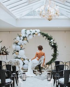 a woman is sitting in a room with black chairs and white balloons on the ceiling