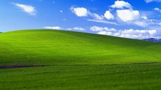 a green field with blue sky and clouds in the background is seen from across the valley