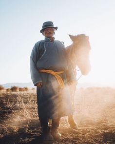 a man standing in the middle of a field with a horse on his back and sun shining behind him