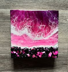 a pink and white painting on top of a wooden table next to a black box