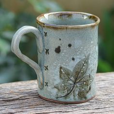 a coffee mug with a butterfly design on it sitting on a wooden table outside in the sun